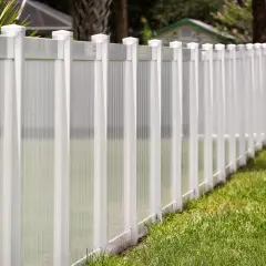 A newly completed vinyl fence installation, featuring white posts and translucent panels, lines a lush green lawn.