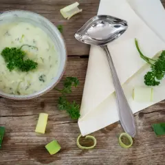 Kremowy sos porowy z natką pietruszki, podany w misce, obok łyżki i kawałków pora.