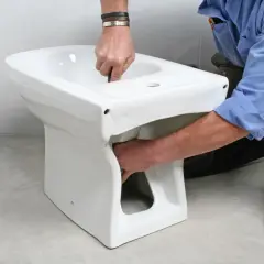 Instalator montuje białą ceramikę, pokazując, jak podłączyć bidet.