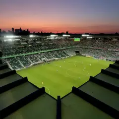 Zachód słońca nad stadionem Legii. Widok z góry na murawę, trybuny wypełnione kibicami i panoramę Warszawy. Pojemność stadionu Legii robi wrażenie.