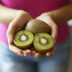 Dłonie trzymają całe i przekrojone kiwi. Ten owoc to naturalny sposób na zaparcia.