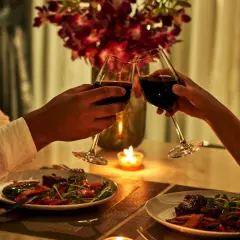Romantyczna kolacja dla dwojga przy świecach. Dwie pary kieliszków z czerwonym winem unoszą się w geście toastu.