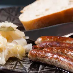 Herzhaftes Sauerkraut mit vier goldbraunen Würsten und einem Stück Brot auf einem dunklen Teller.