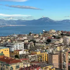 A panoramic view of Naples in December, with the blue sea and distant mountains under a cloudy sky.