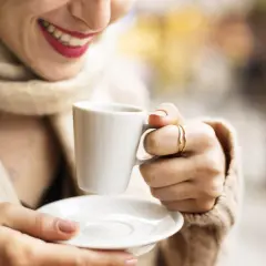 Donna sorride tenendo una tazzina di caffè. Speriamo non sia troppo acquoso, come a volte capita con la macchina del caffè.
