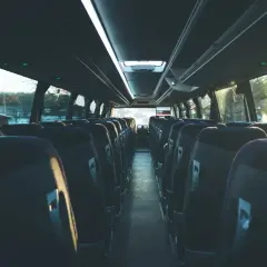 Puste siedzenia w autobusie, gotowe na podróż. Widać rząd siedzeń po obu stronach, sugerując, że busy są wieloosobowe.