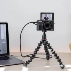 Configuración para usar webcam como cámara de seguridad: una Canon G7X en un trípode flexible, conectada a un portátil que muestra a un hombre sonriendo.