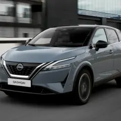 Grå Nissan Qashqai kör på en väg, en del av ett nissan qashqai test. Moderna byggnader syns i bakgrunden.