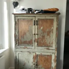 Vieil armoire en bois patiné, prêt à être customisé. Une baguette repose sur le dessus.