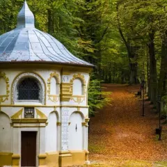 Kaplica na Kalwarii Kaszubskiej w jesiennej scenerii, otoczona drzewami i ścieżką usłaną liśćmi.