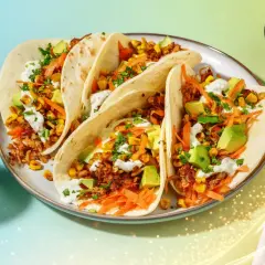 Här är en tallrik med pulled pork tacos, fyllda med majs, avokado och strimlad morot, toppade med en krämig sås.