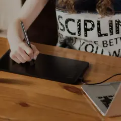 Osoba rysuje na tablecie graficznym, który służy do cyfrowego tworzenia grafiki i ilustracji, podłączonym do laptopa.