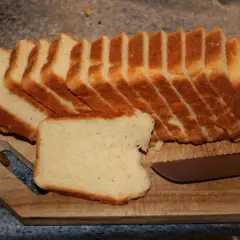 Tranches de pâte à pain de mie dorées et moelleuses, prêtes à être dégustées sur une planche en bois avec un couteau.