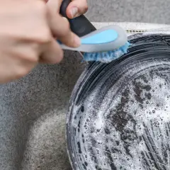 Ręka szoruje przypaloną patelnię z zewnątrz gąbką z pianą. Dowiedz się, jak wyczyścić przypaloną patelnię z zewnątrz.