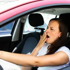 Mujer bosteza al volante, un claro ejemplo de qué puede causar somnolencia en un conductor.