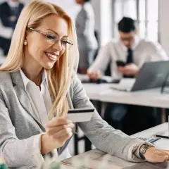 Uśmiechnięta kobieta z kartą płatniczą w ręku, korzystająca z laptopa. To idealne rozwiązanie dla spółki z o.o. do zarządzania finansami.