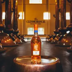 Bouteille de whisky Glenmorangie 18 ans posée sur un plateau en cuivre, au cœur de la distillerie Glenmorangie, entourée d'alambics en cuivre.