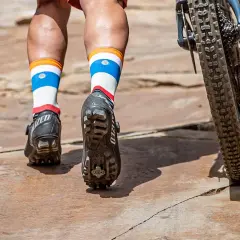 Mountain biking shoes with cleats are shown, not hiking boots. The rider's colorful socks and bike tire are also visible.