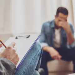 Rozmowa z terapeutą o trudnym rozwodzie z osobą chorą psychicznie. Mężczyzna w rozpaczy, terapeuta notuje.