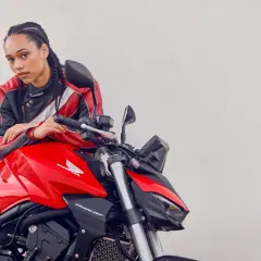 Joven con chaqueta de cuero posa junto a una moto roja Honda Hornet. Lista para el rodaje moto 125.