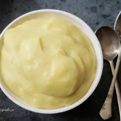 Gładki, żółty krem patissiere w białej miseczce, obok dwie łyżeczki. Idealny do deserów.