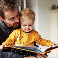 Ojciec czyta dziecku książkę, wspierając jego pierwsze kroki w nauce czytania.