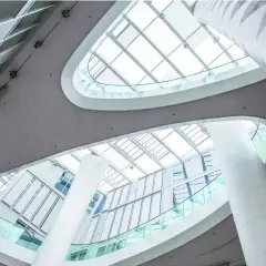 Nowoczesne wnętrze z białymi kolumnami i szklanymi balustradami, przez które wpada obfite światło dzienne.