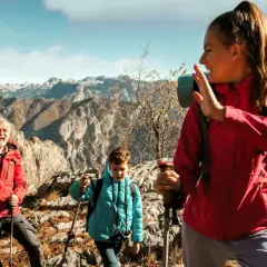 Familia disfrutando de la vista en la montaña, con ropa adecuada para la montaña y equipo de senderismo.