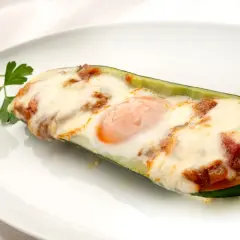 Deliciosos calabacines rellenos con huevo y queso gratinado, adornados con perejil fresco.