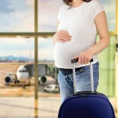 Kobieta w pierwszym trymestrze ciąży z walizką na lotnisku, w tle samolot.