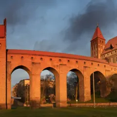 Imponujące zamki na Pomorzu, z cegły i czerwonym dachem, oświetlone zachodzącym słońcem, na tle burzowego nieba.