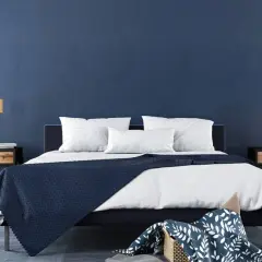 Ein modernes Schlafzimmer mit tiefblauen Wänden, die Ruhe und Harmonie ausstrahlen – eine ideale feng shui schlafzimmer farbe. Weiße Bettwäsche und dunkle Akzente schaffen ein stilvolles Ambiente.