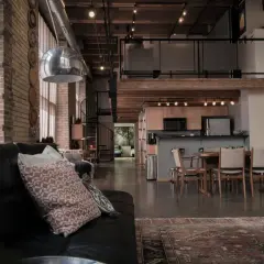 A spacious industrial loft with exposed brick, a spiral staircase, and a modern kitchen.