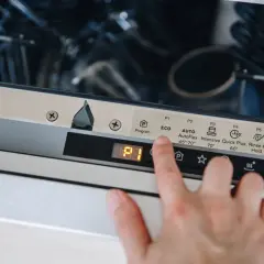 Dłoń naciska przycisk "Reset" na panelu zmywarki Electrolux, co może być pierwszym krokiem, jak zresetować zmywarkę electrolux.