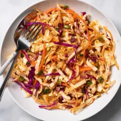 En skål med krispig kål, morötter och rödlök, perfekt för ett enkelt coleslaw recept. En gaffel och sked ligger i skålen.