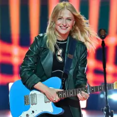 Uśmiechnięta piosenkarka z blond włosami gra na niebieskiej gitarze. Jedna z wielu utalentowanych polskich piosenkarzy na scenie.