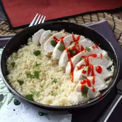 Delizioso pollo in padella a fette, servito su un letto di couscous e guarnito con prezzemolo e salsa piccante.