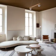 Salotto moderno con divano curvo, tavolini dalle forme organiche e un camino. Le pareti e il soffitto stesso colore creano un'atmosfera avvolgente.
