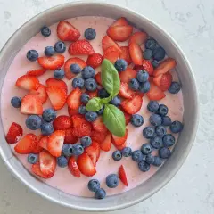 En läcker vegansk jordgubbstårta i en form, toppad med färska jordgubbar, blåbär och en kvist basilika.