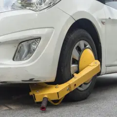 Ruota anteriore di un'auto bianca bloccata da un dispositivo giallo, segno di confisca veicolo.