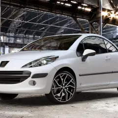 Vit Peugeot 207 cabriolet med snygga fälgar i en övergiven lagerlokal. Inga problem här, bara stil!