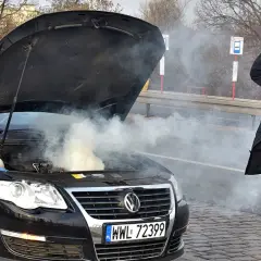 Zmartwiony kierowca przy dymiącym silniku. Zastanawia się, ile kosztuje wyjęcie silnika z samochodu po awarii.