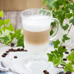 Warstwowe latte w szklance, otoczone bluszczem i ziarnami kawy. Prosty sposób, jak zrobić latte bez ekspresu.
