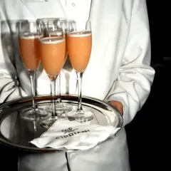 Kellner serviert Bellinis auf einem Silbertablett. So trinkt man Bellini: ein erfrischender Cocktail aus Prosecco und Pfirsichpüree.