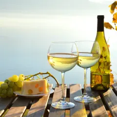 Dwa kieliszki białego wina, butelka, winogrona i ser na drewnianym stole. Idealne na wieczór, gdy liczymy wino białe kcal.