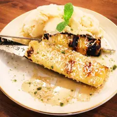 Grillad ananas på spett, toppad med kokosflingor, serveras med vaniljglass och en myntakvist. En härlig dessert!