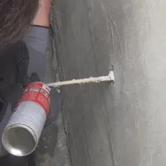 Mit Montageschaum wird ein kleines bohrloch abgedichtet. Die Dose wird gehalten, während der Schaum in das Loch gesprüht wird.