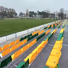 Puste trybuny stadionu Lechii Zielona Góra, z rzędami zielonych i żółtych krzesełek, czekają na kibiców.