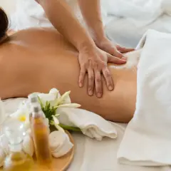 Mains expertes prodiguant un massage américain relaxant sur le dos huilé d'une femme, avec des fleurs de frangipanier et des huiles de massage à proximité.