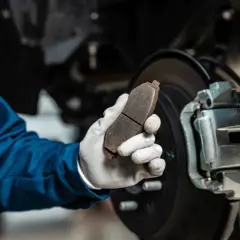 Mechanik w niebieskim kombinezonie trzyma zużyty klocek hamulcowy, zastanawiając się, ile kosztuje wymiana zacisku hamulcowego.